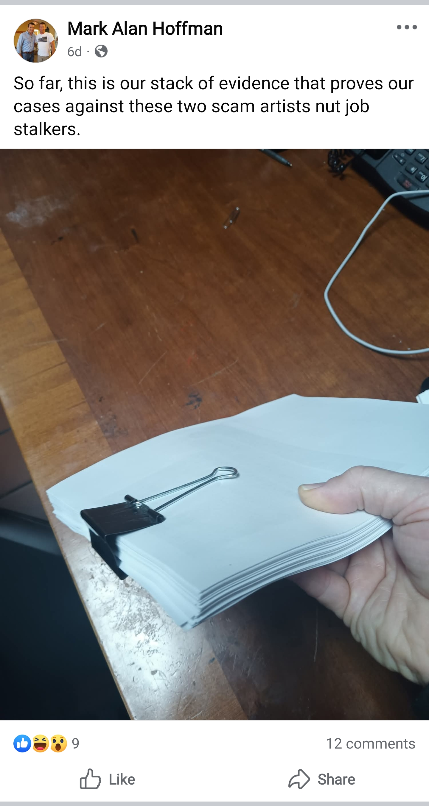 Screencap of a Facebook post saying: “So far, this is our stack of evidence that proves our cases against these two scam artists nut job stalkers.”  Attached to the post is a disembodied hand holding a stack of papers held together with a large binder clip; no text is visibile on said paper.  The post has nine reactions and twelve comments.